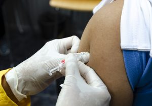 Doctor giving patient vaccine, flu or influenza shot or taking blood test with needle. Nurse with injection or syringe. Medicine, insulin or vaccination. Hospital office room.