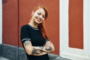Portrait of smiling red-haired tattooed woman standing in the city