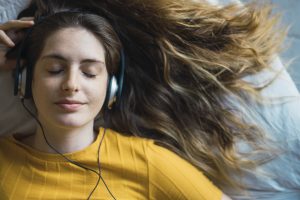 Portrait of smiling young woman lying on bed listening music with headphones
