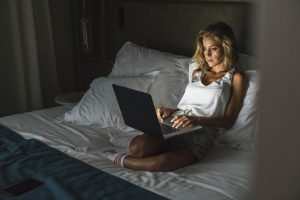 Woman sitting on bed, using laptop