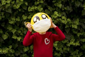 Little girl with an emoticon ball with a medical mask in front of an ivy 03