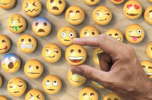 Many wooden emoticon or Emoji face balls, hand holding one