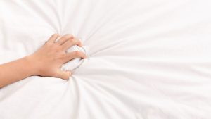 Female hand grasping white crumpled bed sheet