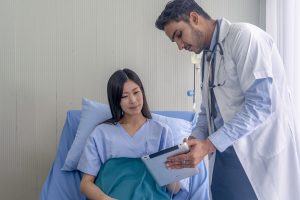 Handsome doctor is talking with young female patient and making notes while in his office