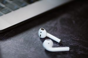 White AirPods EarPods near a laptop with black background