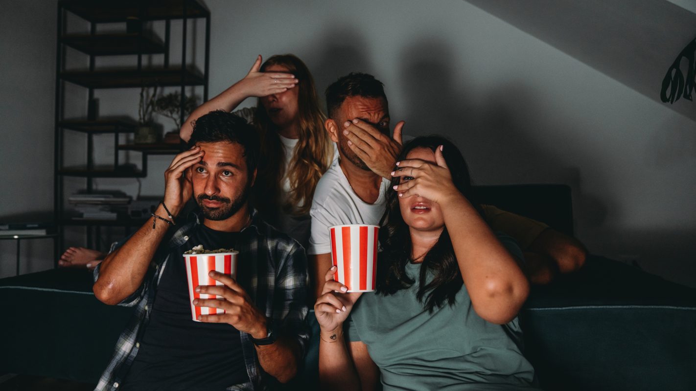 Un grupo de cuatro amigos están viendo la televisión en casa mientras comen palomitas de maíz. (Foto vía Getty Images)
