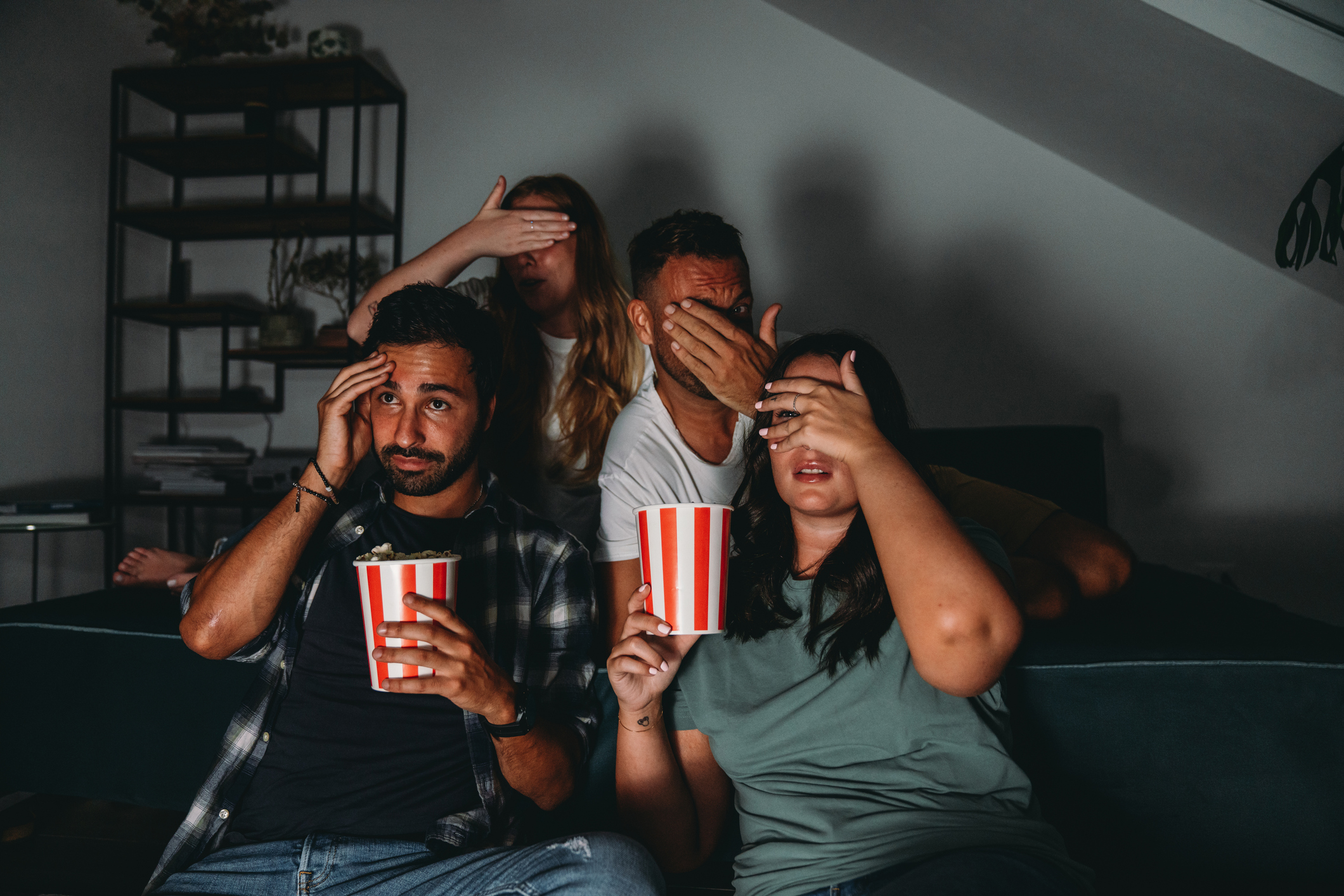 Un grupo de cuatro amigos están viendo la televisión en casa mientras comen palomitas de maíz. (Foto vía Getty Images)